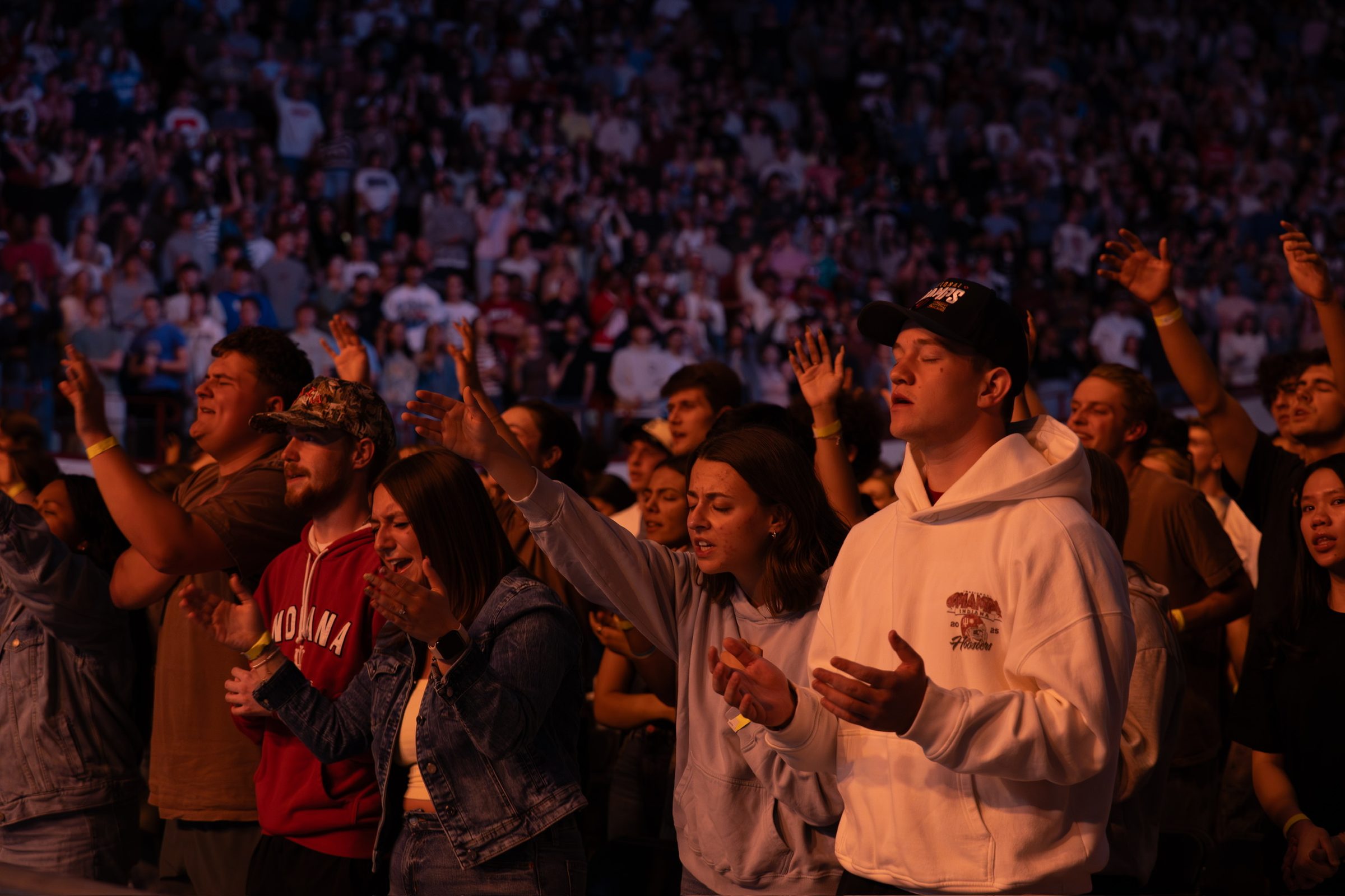 A standing crowd bathed in amber stage light, hands raised, eyes closed